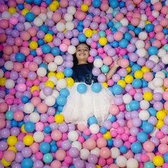 The pure, uninhibited joy of childhood captured as a young girl lies back in a colorful ball pit during her birthday celebration. This playful portrait is full of vibrant colors and happy energy.