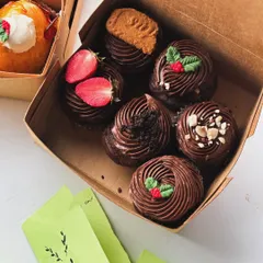 A Christmas-themed box of assorted chocolate cupcakes with festive toppings.