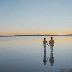 A beautiful silhouette of a couple walking hand-in-hand into the sunset on a Turkish salt flat. The reflection in the water and the vast, open sky create a feeling of infinite love and endless possibilities.
