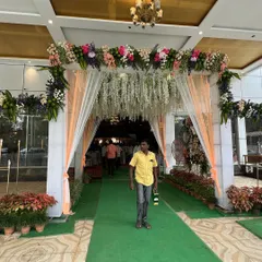 A lovely floral entrance arch for a wedding hall. The combination of pastel-colored flowers, hanging white floral strings, and soft peach drapes creates an elegant and inviting look.