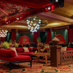 A luxurious lounge setting within the Sufi Durbar. A red velvet chaise lounge sits on a richly patterned carpet, surrounded by custom-designed partitions and emerald green backdrops, creating an intimate space for conversation.