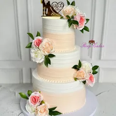A classic three-tier wedding cake that exudes timeless romance. The soft ombre buttercream is adorned with clusters of delicate blush and ivory roses, and a sweet silhouette topper completes the look.