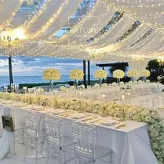 This all-white reception setup by the sea is the essence of elegance. I used white floral runners, transparent ghost chairs, and a ceiling of draped fabric with fairy lights to create a breathtaking, monochromatic look.