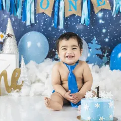 A big, happy smile from the birthday boy at his winter-themed cake smash. The blue tie and snowflake cake create a cool and fun first birthday photo.