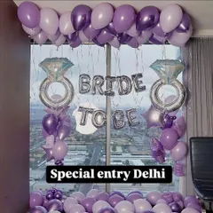A fun and feminine 'Bride to Be' room decoration. This setup uses shades of purple balloons, large diamond ring foil balloons, and a city view from the window as a backdrop.