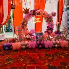 A grand first birthday setup for "Trishaan" in an outdoor tent setting. This decoration includes a circular balloon arch, the baby's name in foil letters, and a "Happy Birthday" neon sign.