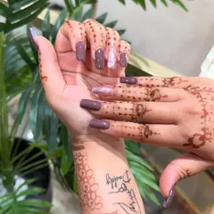 These long, square-shaped nail extensions provide a large canvas for both solid colors and art. Here they are shown in a solid mauve color with a single silver glitter accent nail, complementing the client's henna.