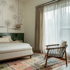 A beautiful, light-filled bedroom featuring a custom wall mural of palm trees. The low-slung bed, colorful rug, and woven accent chair create a space that feels like a breezy, tropical retreat.