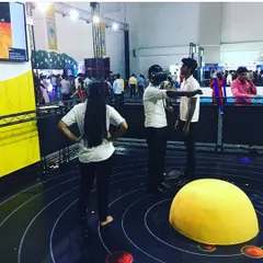A VR station set up at a large exhibition, drawing a crowd of onlookers and participants. The open design with a solar system floor graphic creates an inviting space for guests to explore virtual worlds.