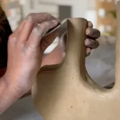 A student smoothing the edges of a complex, multi-spout vase. Hand-building is all about patience and precision.