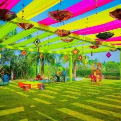 This outdoor Mehendi decor in Noida features a vibrant canopy of yellow, pink, and green drapes with hanging umbrellas. The open lawn setting is perfect for a fun, daytime celebration.