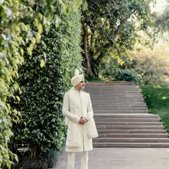 A handsome portrait of the groom in his elegant all-white sherwani, standing in a lush green garden. A timeless and regal shot.