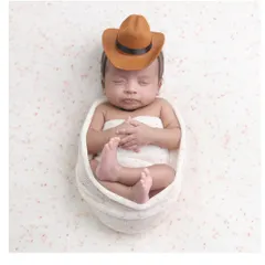 A little cowboy in a simple setup. The focus remains on the baby's adorable pose and tiny cowboy hat in this minimalist portrait.