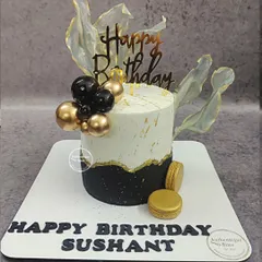 A classy black and gold birthday cake with macarons and translucent sails. This modern design is perfect for a sophisticated milestone celebration.