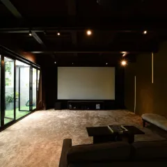 This home theater opens up to a garden through floor-to-ceiling glass doors, blending entertainment with nature. The dark, moody interior with plush carpeting and a large screen is perfect for movie nights.