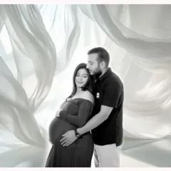 An intimate black and white couple portrait. This studio shot uses soft, flowing fabric in the background to create a dreamy, ethereal feel, focusing on the connection between the parents-to-be.