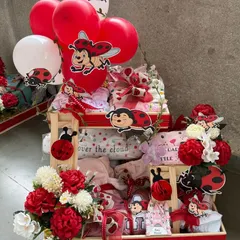 An adorable "ladybug-themed" baby hamper, perfect for a baby girl. This tiered arrangement is filled with clothing, essentials, and cute ladybug cutouts, all in a vibrant red and white color scheme.