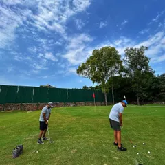 Two friends work on their chipping and pitching on our real turf short game area under a beautiful blue sky.
