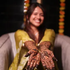 A joyful bride showing her palms, each telling a different part of her story through custom portrait mehendi.