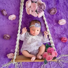 A dreamy swing setup for a baby girl, surrounded by a cascade of purple and pink flowers. The soft, plush rug adds to the magical, garden-like feel.