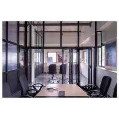 A view into the conference room, which features a flexible folding partition. The design uses black metal frames and glass to maintain visual openness while allowing for private meetings.