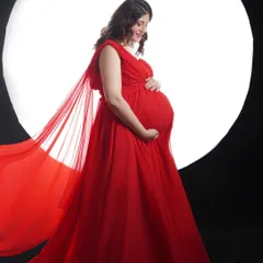 A silhouette of love against the moon. This dramatic studio portrait uses bold lighting and a vibrant red gown to create a powerful and artistic image of motherhood.