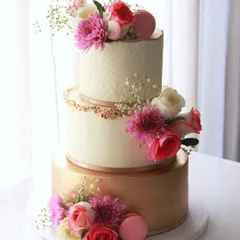 An elegant and minimalist three-tiered engagement cake. The design combines a brushed gold bottom tier, a smooth middle tier, and a stenciled top tier, all tied together with fresh flowers and macarons.