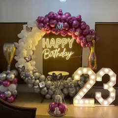 A glamorous 23rd birthday celebration featuring large light-up marquee numbers, a custom "Happy Birthday" neon sign, and a chic balloon arch in magenta, silver, and white with butterfly accents.