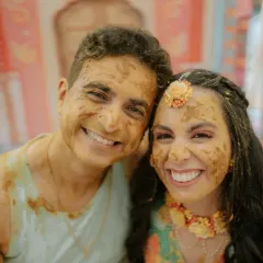 The happy couple smiling for the camera, their faces covered in turmeric paste during their fun and messy Haldi ceremony.