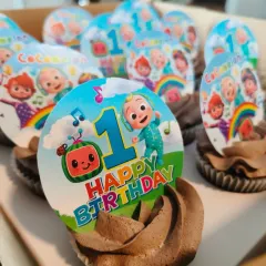 A close-up of the Cocomelon themed chocolate cupcakes I made for a first birthday. Each cupcake has a custom topper featuring characters from the show, making them a perfect party favor.