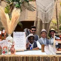 Our team of bartenders, dressed in smart vests and hats, posing behind the completed bohemian bar. The setup includes pampas grass, a custom cocktail menu, and rustic decor.