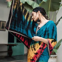 A graceful and elegant shot highlighting the beautiful drape of a tie-dye saree. The model's pose shows off the colorful pallu, creating a sense of movement and artistry.