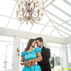 An intimate embrace under a grand chandelier in a bright, airy glasshouse. The natural light floods the scene, creating a soft and romantic ambiance for this elegant couple portrait.