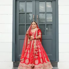 A full length portrait of the bride in her magnificent red lehenga. Standing against a simple, modern doorway, her traditional attire stands out, showcasing its detailed embroidery and grand silhouette.