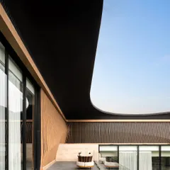 The architecture of Residence Ondra features dramatic, curving rooflines that provide shade and create visual interest. This balcony view showcases the interplay of textures, from the smooth, dark overhang to the vertically slatted wooden walls, creating a private and sheltered outdoor space.