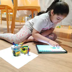 A young girl concentrates as she programs her robotic creation, learning how to translate ideas into commands through coding.