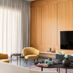 A corner of the living room at Amaiti Farmhouse, showing the interplay of textures. The smooth, cool Kota stone floor contrasts with the warm wood panelling, a soft Persian rug, and plush yellow armchairs, creating a balanced and inviting space.