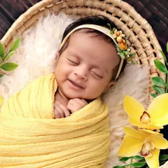 A beautiful, genuine smile from a sleeping baby, surrounded by sunny yellow flowers in a woven basket. This is pure newborn bliss.