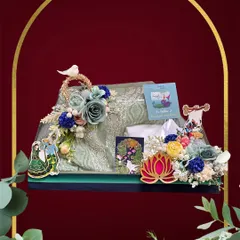 A beautiful Teej hamper featuring a gracefully packed saree. The arrangement is decorated with blue and yellow flowers, a small bird figurine, and traditional Indian motifs for a festive touch.