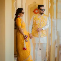 A stylish couple portrait taken during their Haldi event, with both wearing coordinated yellow outfits and sunglasses.