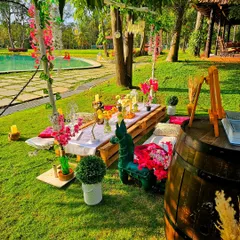 A colorful poolside picnic setup in a lush green resort. The low wooden pallet table is adorned with vibrant flowers, creating a perfect setting for a daytime celebration.