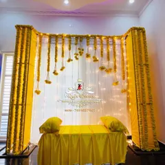 A simple and elegant Haldi ceremony setup for an indoor space. We used a white backdrop with hanging marigold strings and warm fairy lights to create a bright and cheerful ambiance.