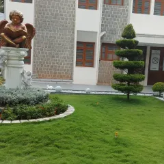 A closer view of the institutional landscape, highlighting a central statue and a spiral topiary tree. These elements serve as focal points in the formal garden design.