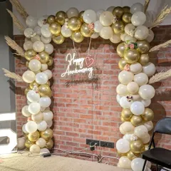 I design elegant backdrops for milestone celebrations like this 25th anniversary. A custom balloon arch in a sophisticated gold and white palette, paired with a 'Happy Anniversary' neon sign, creates a beautiful photo corner.