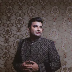 A handsome portrait of the groom in his intricately designed bandhgala, set against a classic patterned wallpaper.