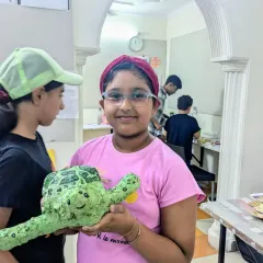 A student proudly holds her completed papermache turtle. She did a fantastic job sculpting the shell and painting it with realistic colors and textures.