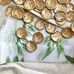A collection of custom gold wax seals, each stamped with the couple's initials. These were used to seal delicate vellum wraps around the invitations, adding a classic and personal touch.