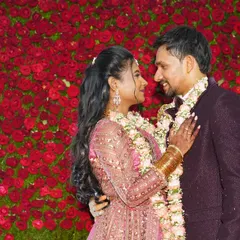A candid moment of a couple sharing a look in front of a stunning wall of red roses at their wedding reception.