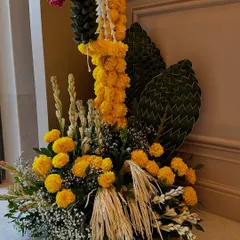 A beautiful floor arrangement for a housewarming, combining vibrant marigolds with woven palm leaves and other traditional greens for a festive and auspicious look.