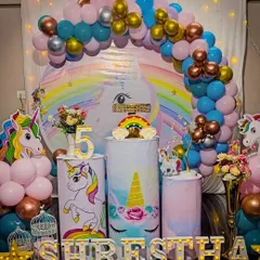 A vibrant unicorn theme for a 5th birthday, featuring a circular backdrop, a light-up number '5', and unicorn-themed plinths for the cake display.